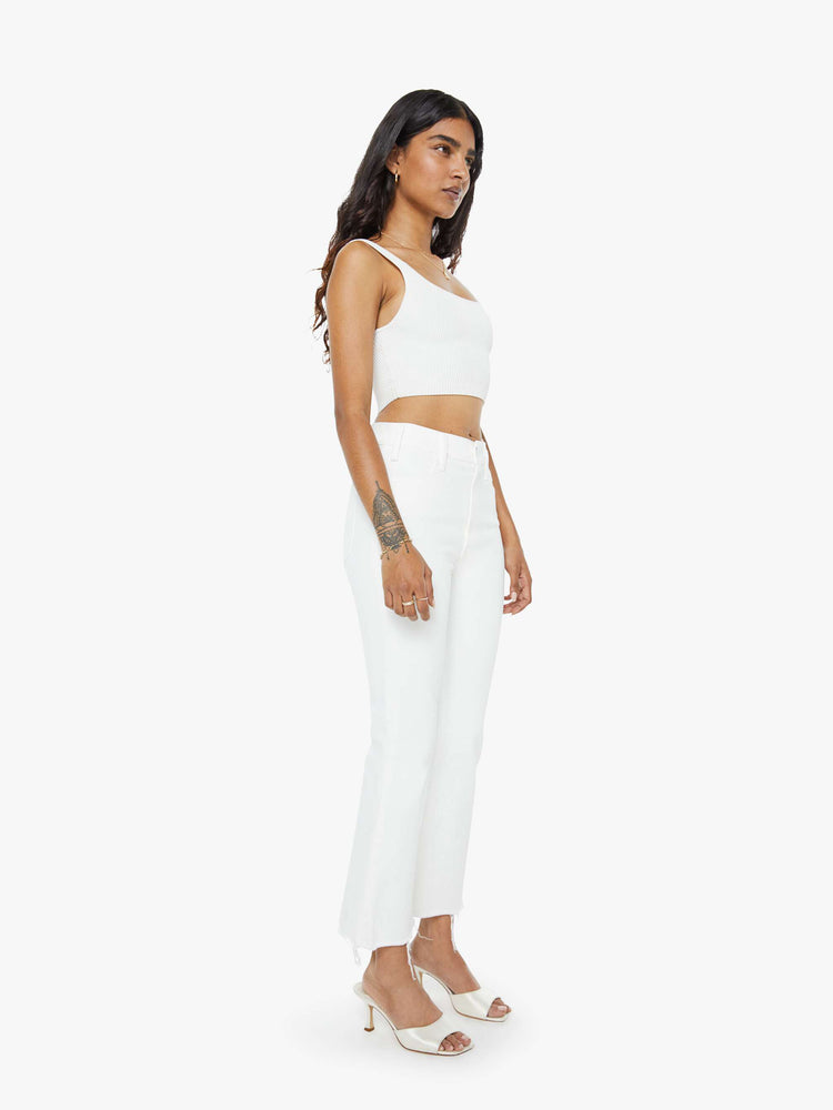 Angled front view of a woman in white  high-rise flare jeans that have an ankle-length inseam and a raw hem. 