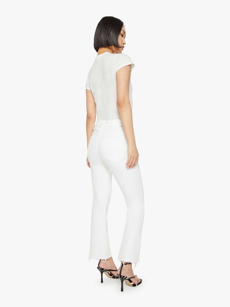 Back view of a woman in white high-rise flare jeans that have an ankle-length inseam and a raw hem.