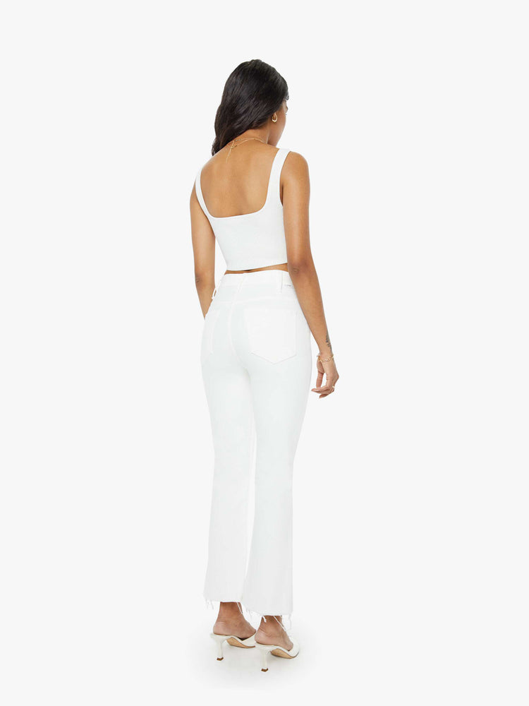 Back view of a woman in white high-rise flare jeans that have an ankle-length inseam and a raw hem.