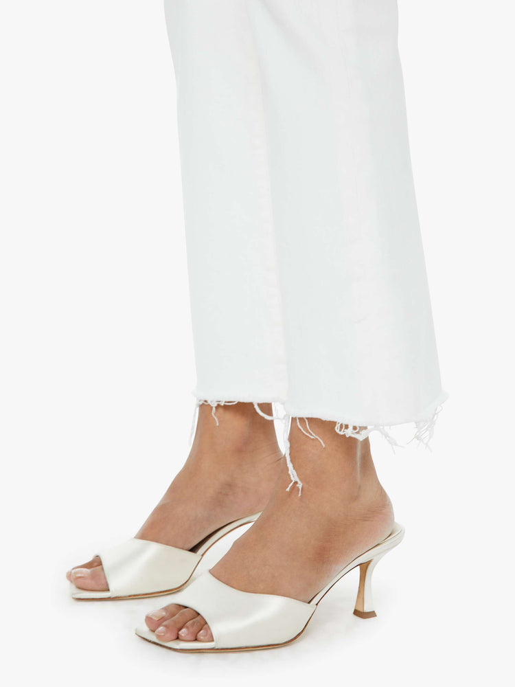 Close up view of a woman in white high-rise flare jeans that have an ankle-length inseam and a raw hem.