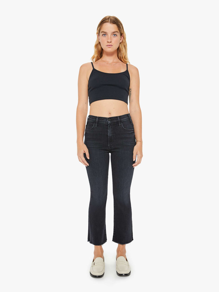 Full body view of a petite womens high-rise flare has an ankle-length inseam and a raw hem in a washed black denim with a subtle white grain.
