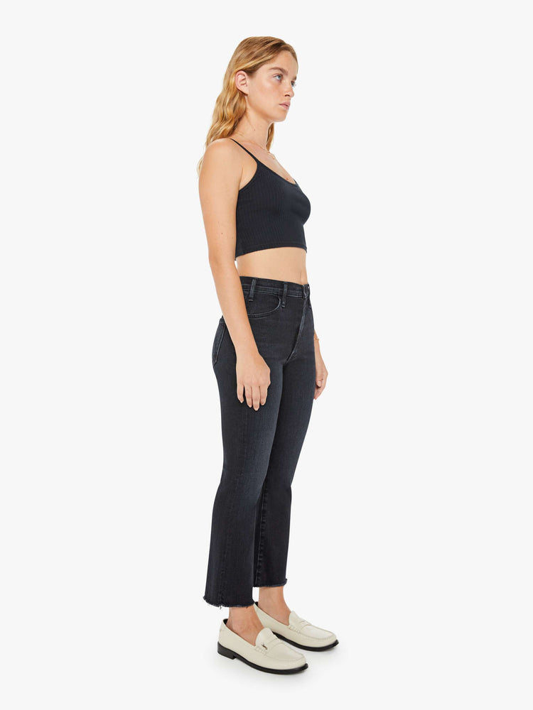 Side angle view of a petite womens  high-rise flare has an ankle-length inseam and a raw hem in a washed black denim with a subtle white grain.