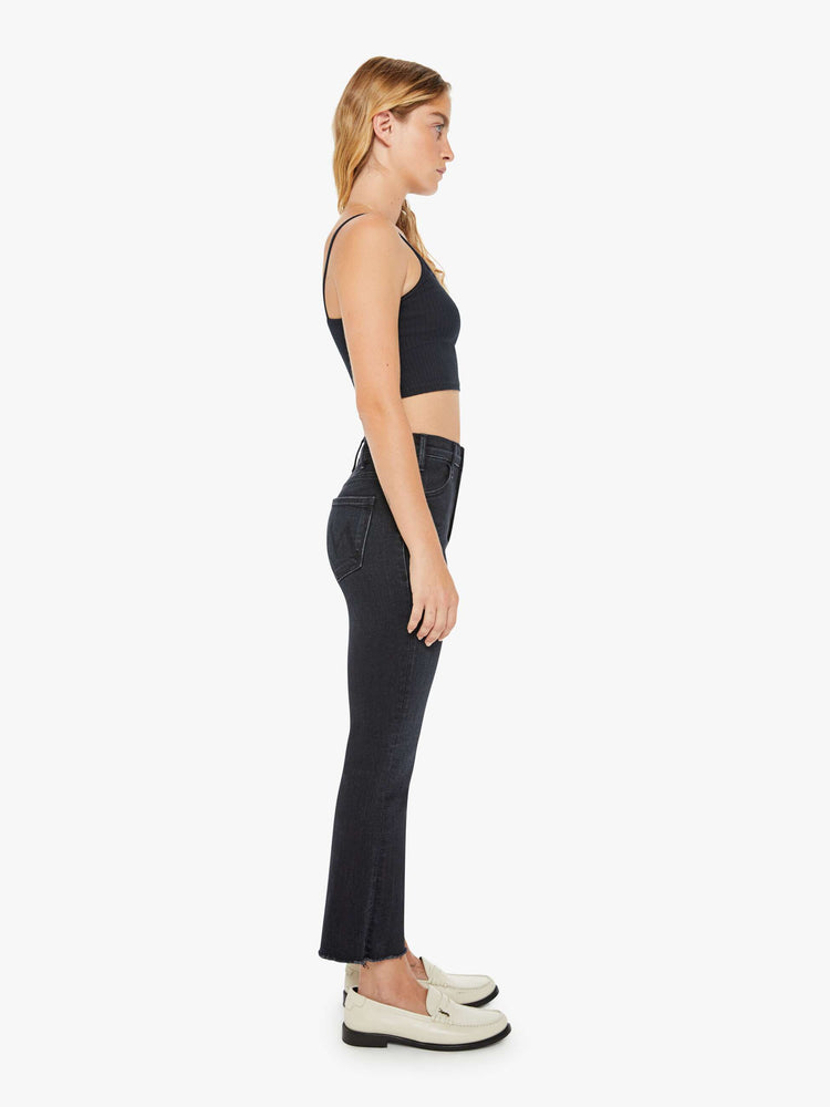 Side view of a petite womens high-rise flare has an ankle-length inseam and a raw hem in a washed black denim with a subtle white grain.