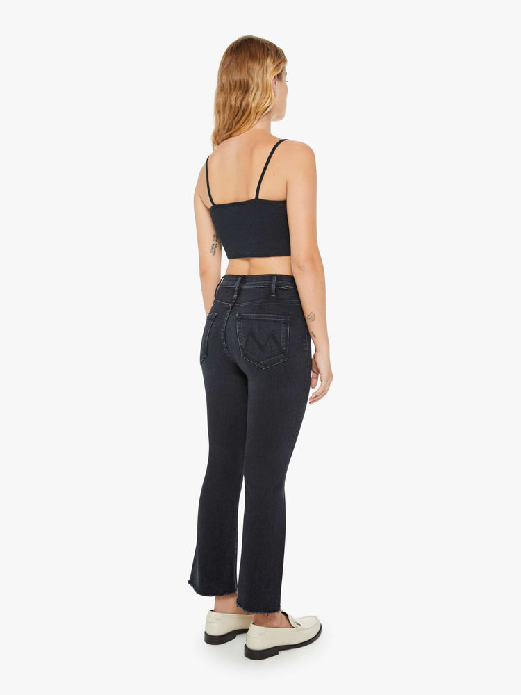 Back view of a petite womens high-rise flare has an ankle-length inseam and a raw hem in a washed black denim with a subtle white grain.