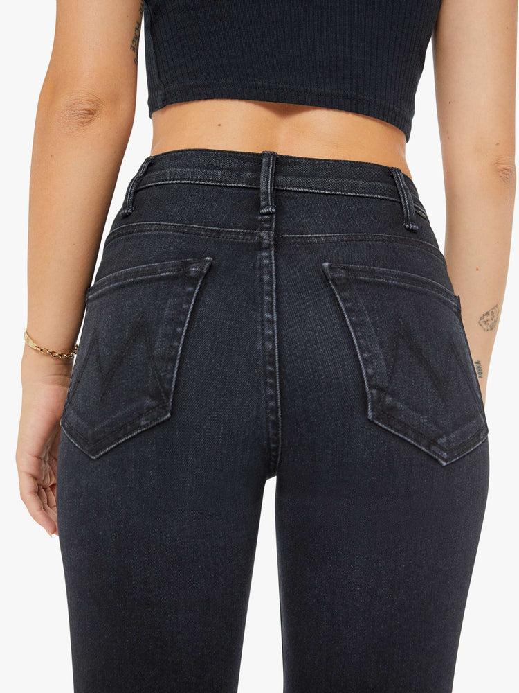 Back close up view of a petite womens high-rise flare has an ankle-length inseam and a raw hem in a washed black denim with a subtle white grain.