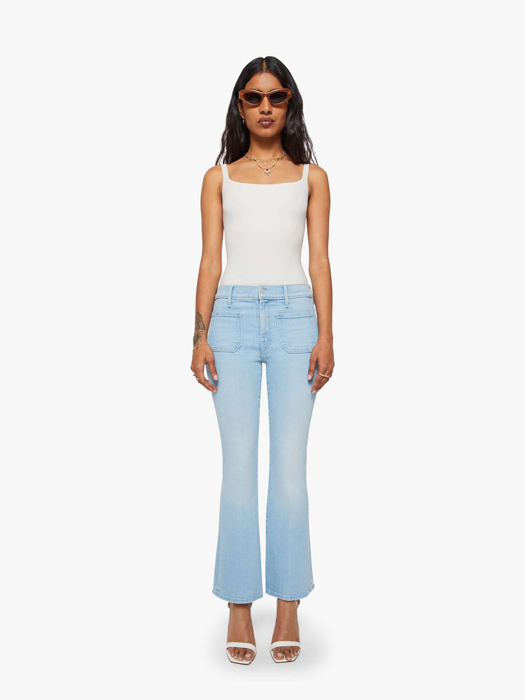 Front view of a petite woman in a light blue flare with a mid rise, zip fly, patch pockets, a 28-inch inseam and a clean hem. 