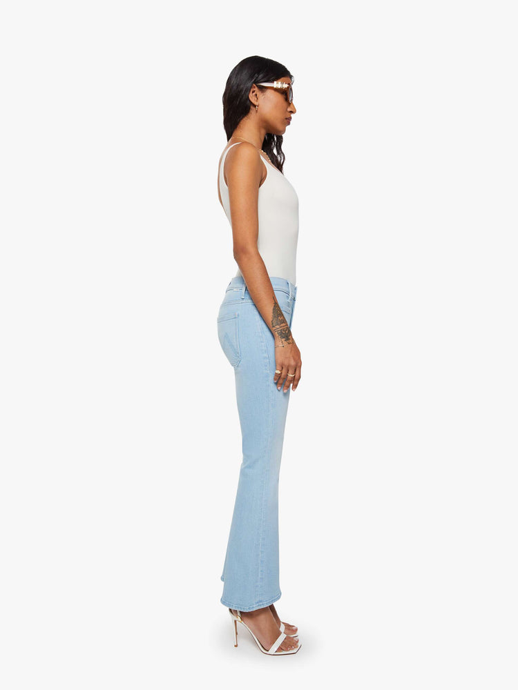 Side view of a petite woman in a light blue flare with a mid rise, zip fly, patch pockets, a 28-inch inseam and a clean hem. 