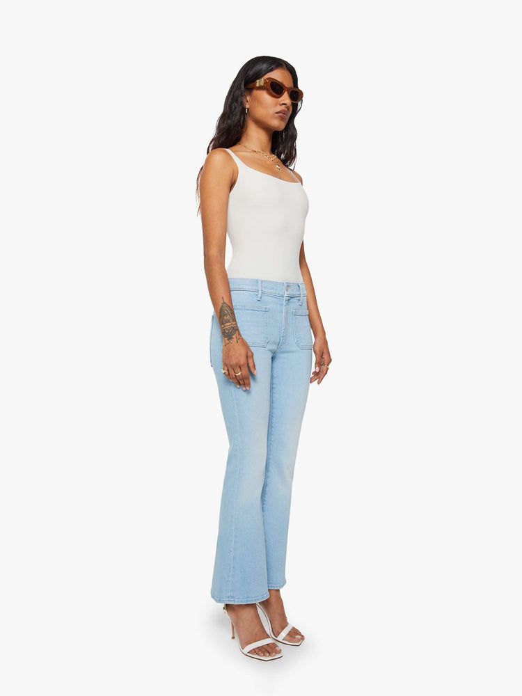 Side angle view of a petite woman in a light blue flare with a mid rise, zip fly, patch pockets, a 28-inch inseam and a clean hem. 