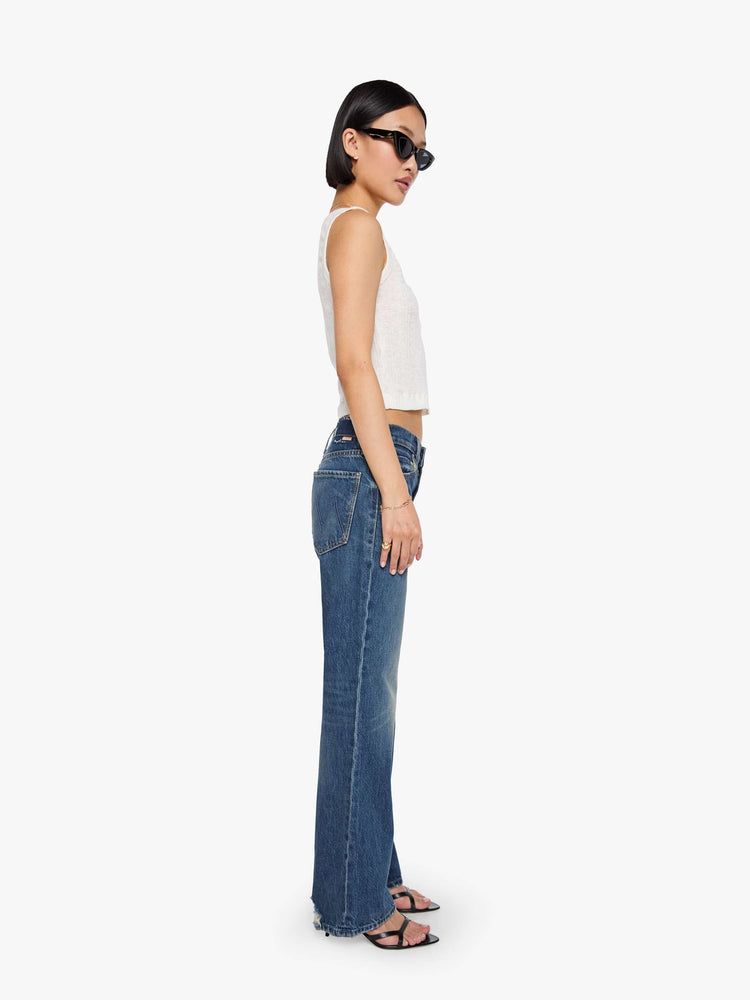 Side view of a petite woman in a  straight leg with a bit of a kick, the jean features a mid rise, full-length inseam and clean hem in a classic blue.