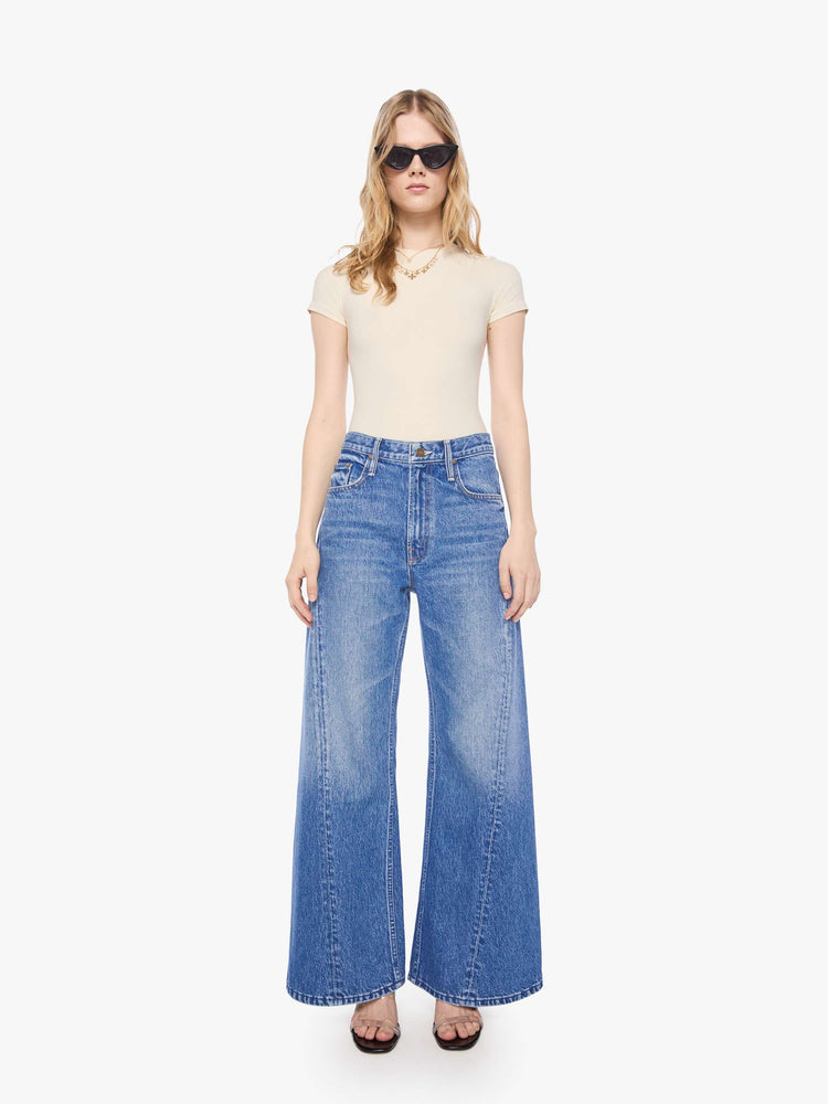 Front view of petite woman in a mid blue high waisted jean with a wide leg  with a curved outer seam and a long 28-inch inseam with a clean hem. 