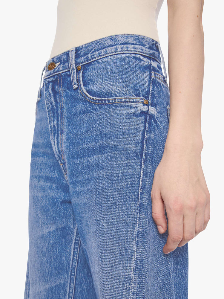 Close up view of petite woman in a mid blue high waisted jean with a wide leg  with a curved outer seam and a long 28-inch inseam with a clean hem. 