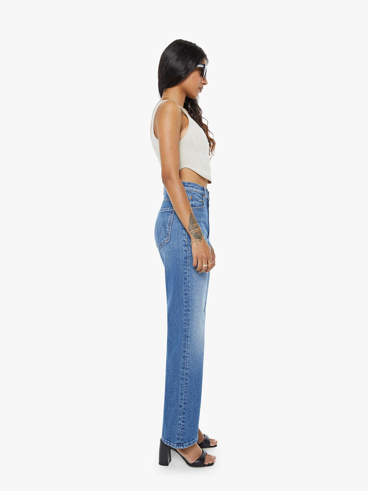 Side view of a petite woman in a med blue high-rise bootcut with a zip fly, looser leg and a long 29-inch inseam with a clean hem.