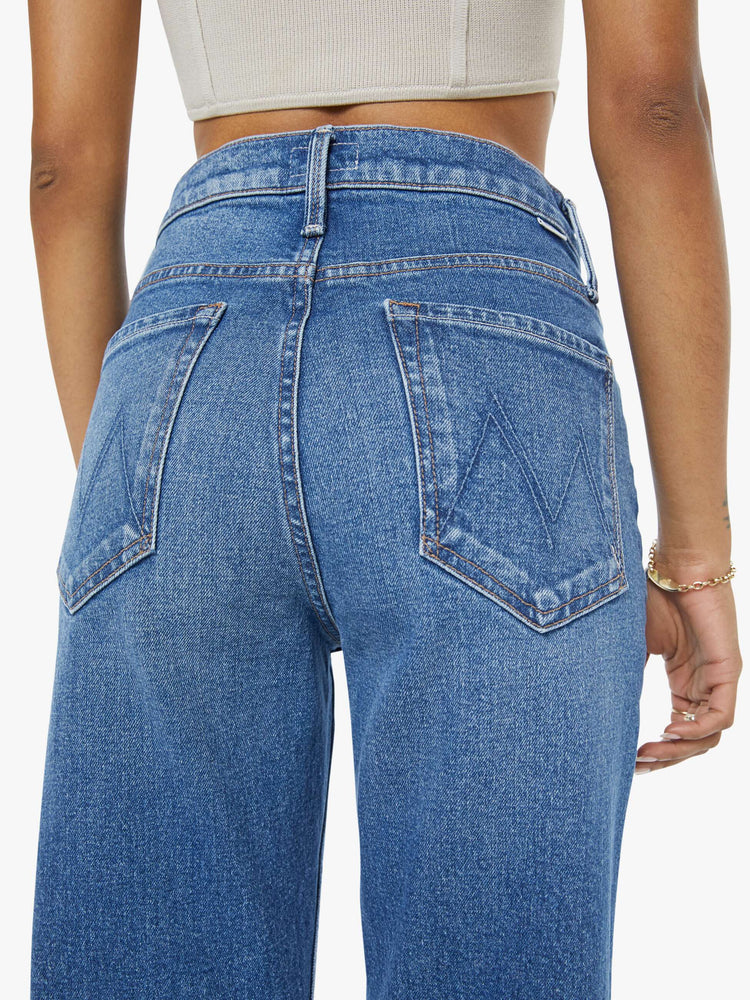 Back close up view of a petite woman in a med blue high-rise bootcut with a zip fly, looser leg and a long 29-inch inseam with a clean hem.