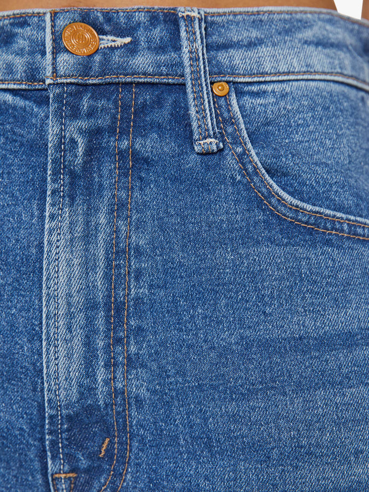 Swatch view of a petite woman in a med blue high-rise bootcut with a zip fly, looser leg and a long 29-inch inseam with a clean hem.