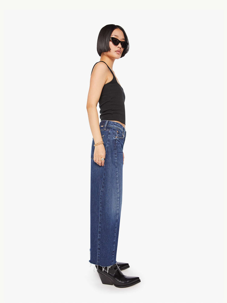 Side view of a petite woman in a mid-rise jeans designed to sit lower on the hips with a full barrel leg, zip fly, 26.25-inch inseam and a frayed hem.