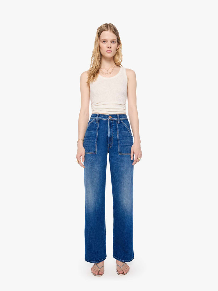 Front view of a woman in a mid blue super high-rise jeans with a loose fit, wide leg, patch pockets, zip fly and 30 3/4 inch inseam with a clean hem.