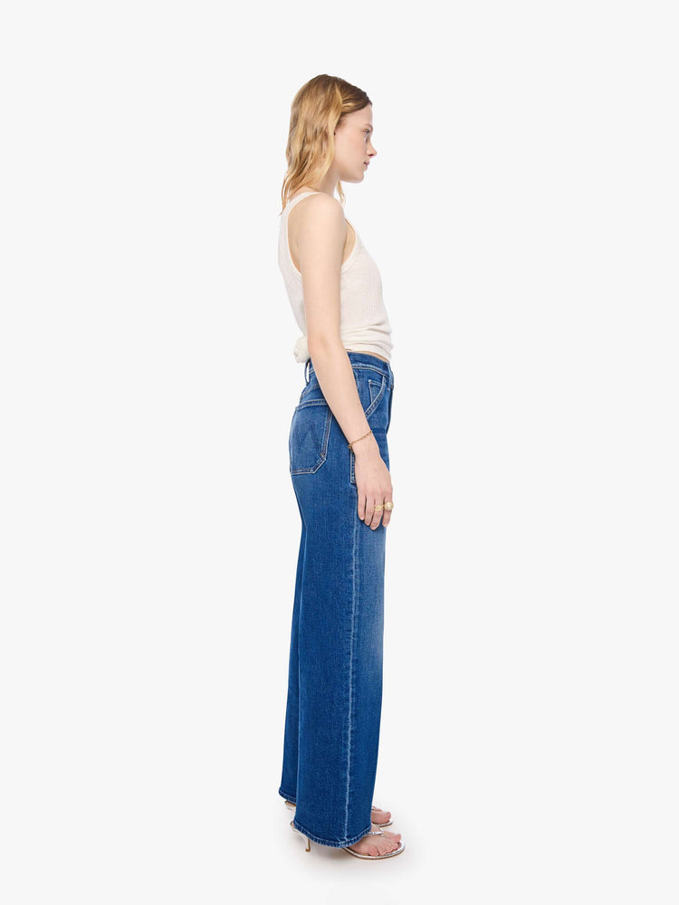 Side view of a woman in a mid blue super high-rise jeans with a loose fit, wide leg, patch pockets, zip fly and 30 3/4 inch inseam with a clean hem.