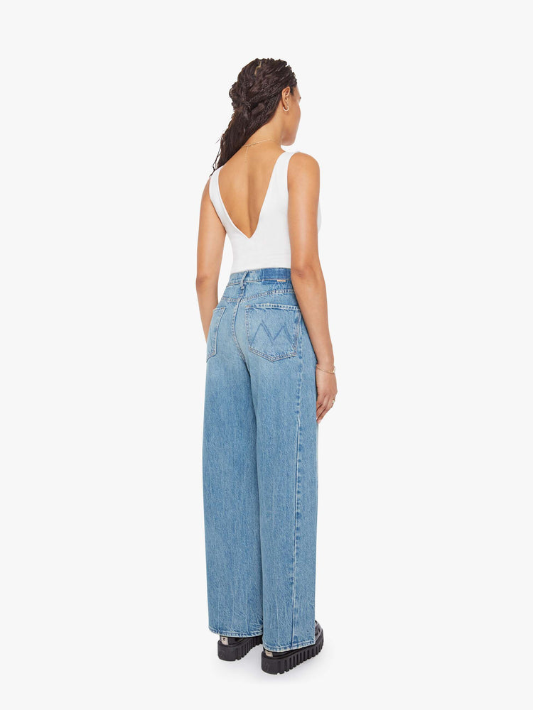 Back view of a woman in a mid blue super high-waisted barrel-leg jeans with a long 30-inch inseam, a button fly, inset panels on the outer seams, a clean hem and relaxed fit. 