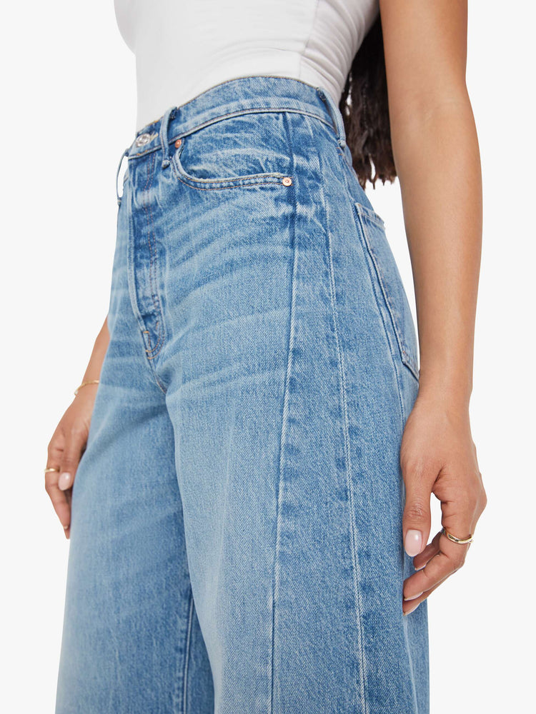 Close up view of a woman in a mid blue super high-waisted barrel-leg jeans with a long 30-inch inseam, a button fly, inset panels on the outer seams, a clean hem and relaxed fit. 