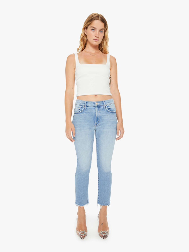 Front view of a petite woman light blue high-waisted bootcut hits at the ankle with a frayed step-hem.