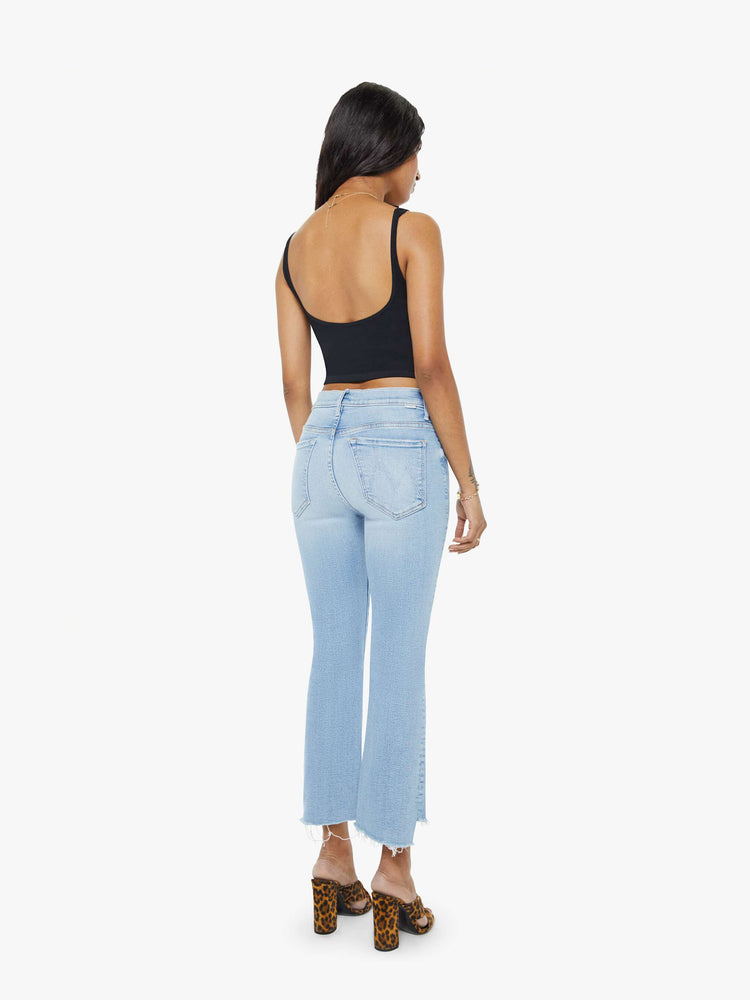 Back view of a petite woman light blue high-waisted bootcut hits at the ankle with a frayed step-hem.