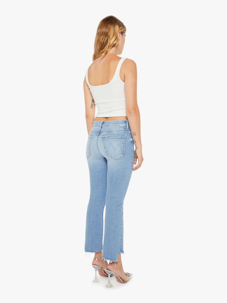 Back view of a petite woman light blue high-waisted bootcut hits at the ankle with a frayed step-hem.