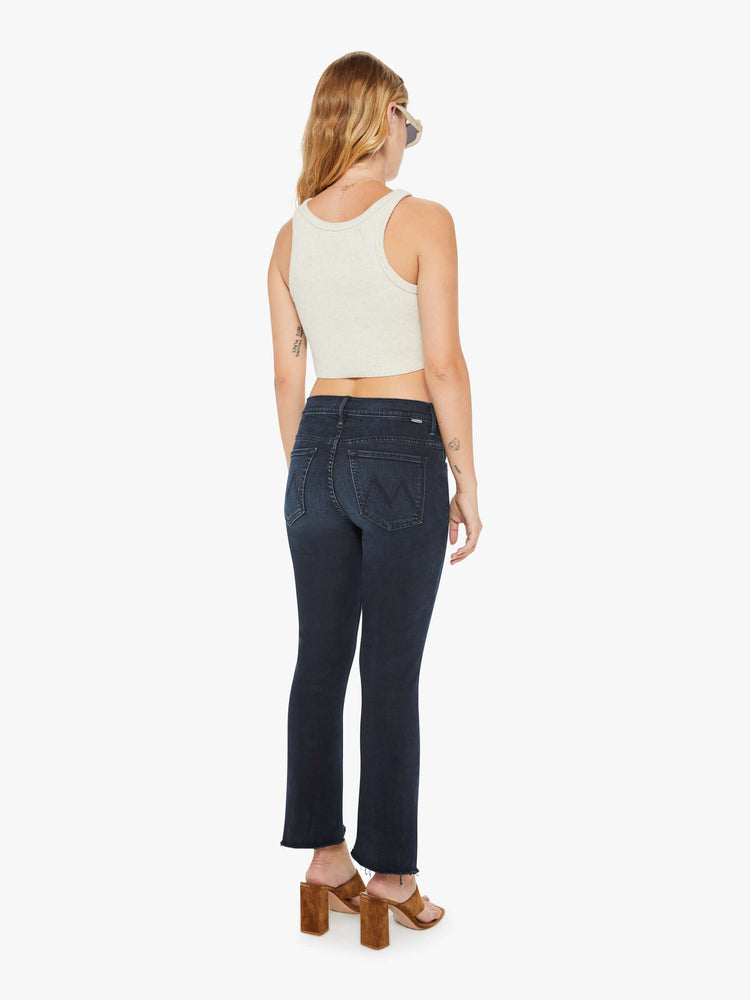 Back view of a petite woman high-waisted bootcut hits at the ankle with a frayed step-hem dark denim jean.
