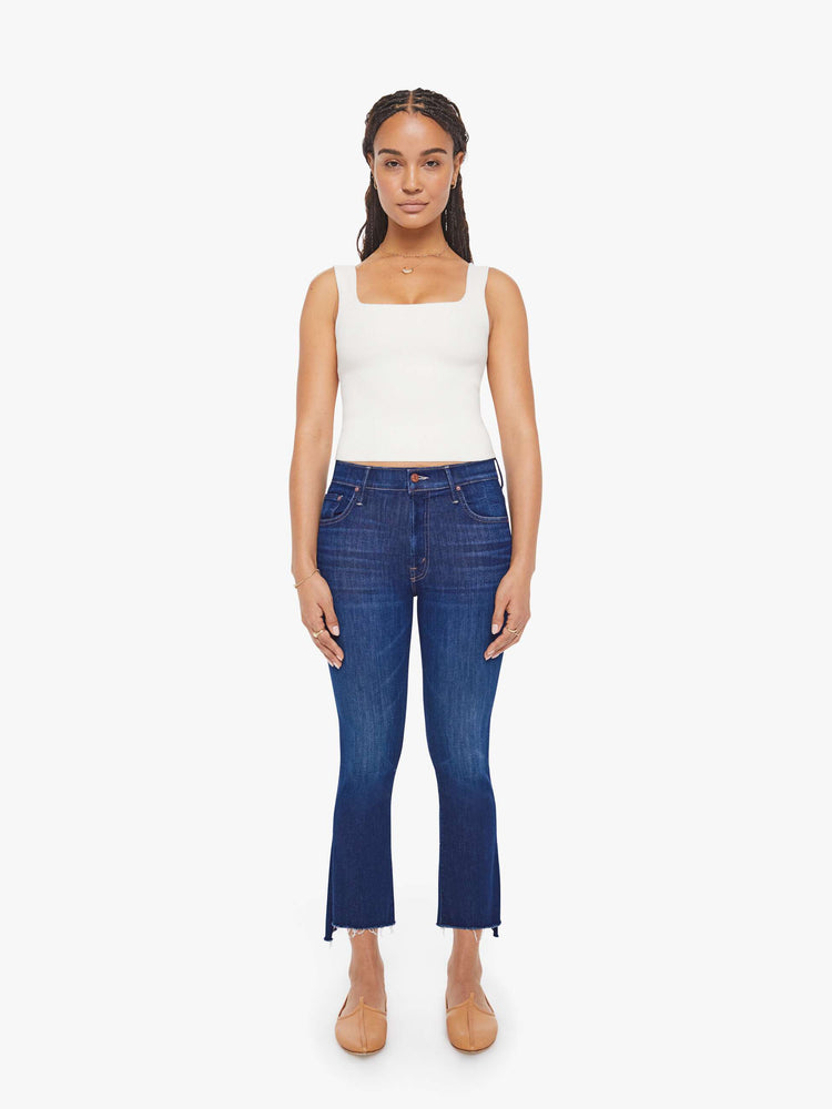 Front view of a petite woman in a dark blue wash high-waisted bootcut is cropped at the ankle with a frayed step-hem jean.