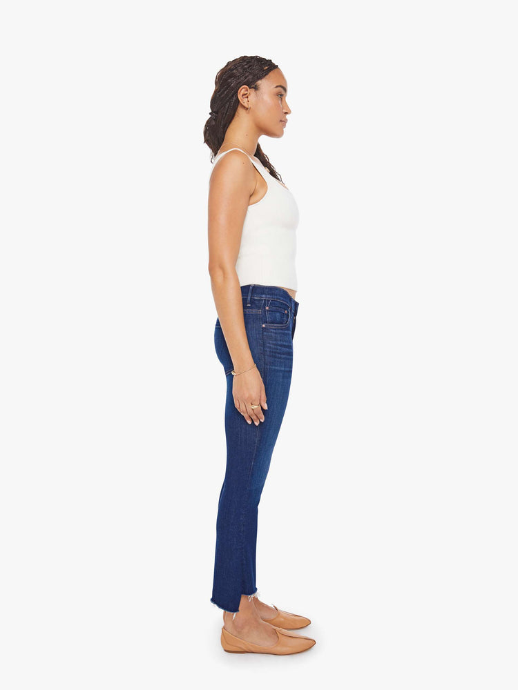 Side view of a petite woman in a dark blue wash high-waisted bootcut is cropped at the ankle with a frayed step-hem jean.