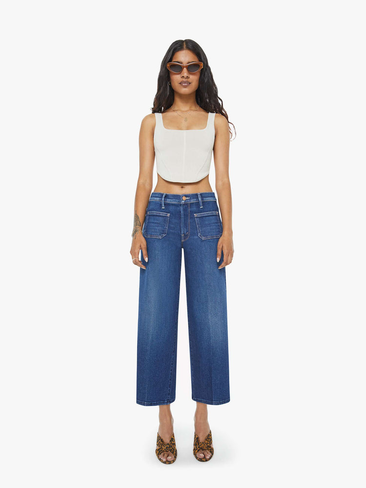 Front view of a woman in a dark blue mid-rise jeans with a loose fit, zip fly, wide leg, patch pockets and ankle-length inseam with a clean hem.