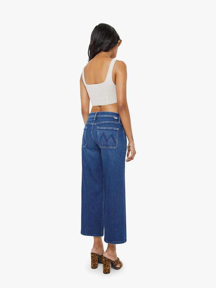 Back view of a woman in a dark blue mid-rise jeans with a loose fit, zip fly, wide leg, patch pockets and ankle-length inseam with a clean hem.