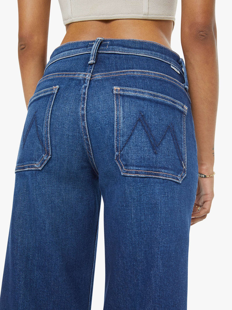 Close up view of a woman in a dark blue mid-rise jeans with a loose fit, zip fly, wide leg, patch pockets and ankle-length inseam with a clean hem.