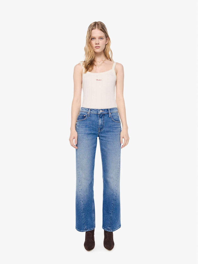 Front view of a petite woman in a mid-blue  mid-rise bootcut with a zip fly, looser leg, twisted outer seam and a long 28-inch inseam with a clean hem. 
