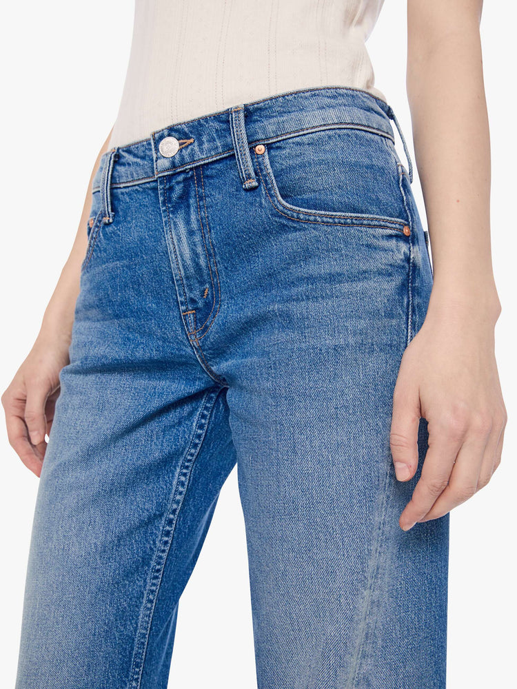 Close up view of a petite woman in a mid-blue  mid-rise bootcut with a zip fly, looser leg, twisted outer seam and a long 28-inch inseam with a clean hem. 
