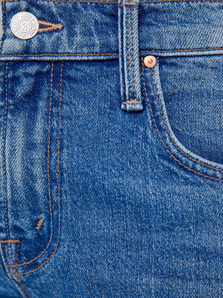 Swatch view of a petite woman in a mid-blue  mid-rise bootcut with a zip fly, looser leg, twisted outer seam and a long 28-inch inseam with a clean hem. 