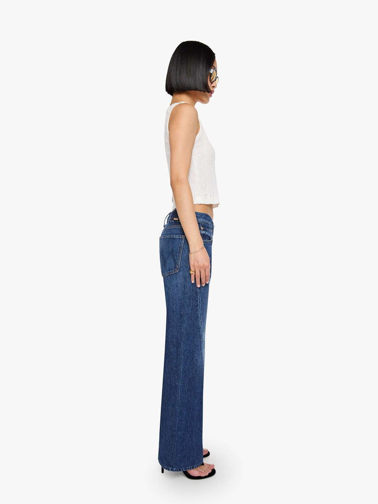 Side view of a petite woman in a mid-rise bootcut with a zip fly, looser leg, twisted outer seam and a long 32-inch inseam with a clean hem.