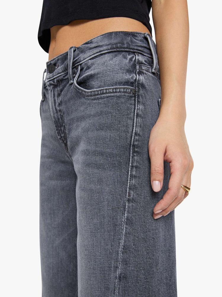 Close up view of a woman in a washed grey mid-rise bootcut with a zip fly, looser leg, twisted outer seam and a long 29-inch inseam with a clean hem.