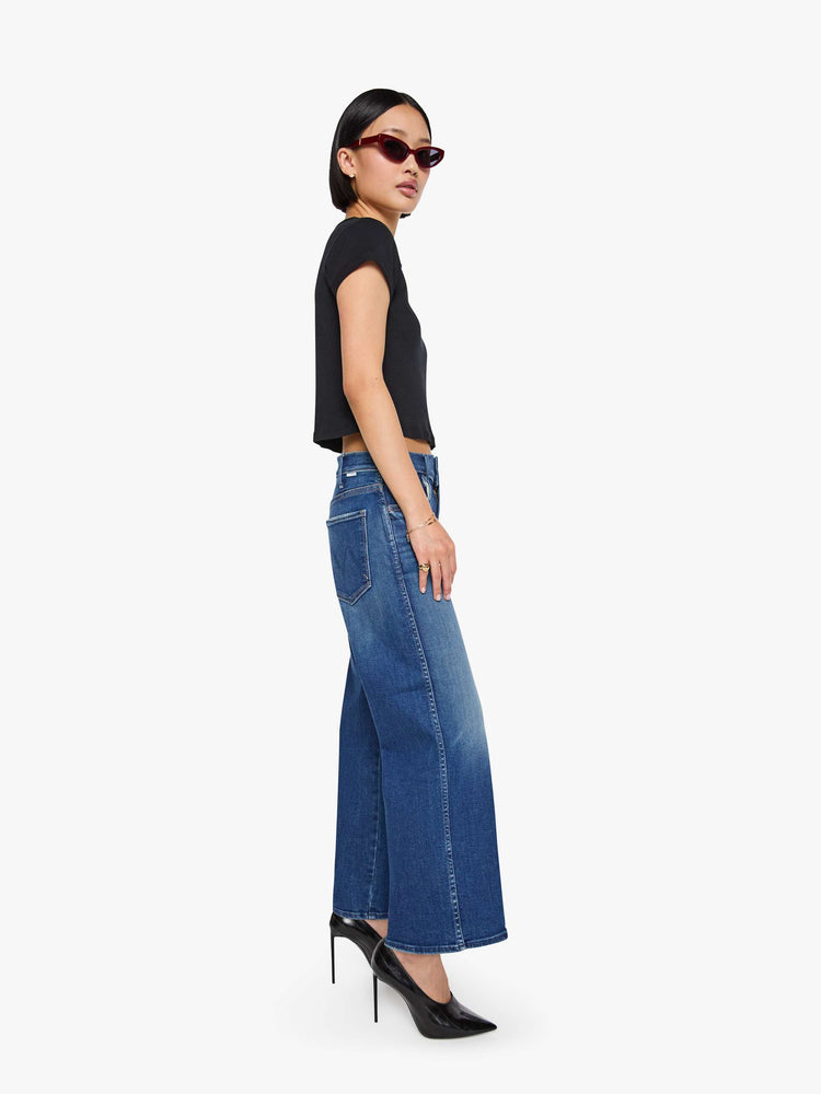 Side view of a petite woman in a med blue wide leg jeans with a high rise, zip fly, double-stitched side seam, 29-inch inseam and a clean hem.