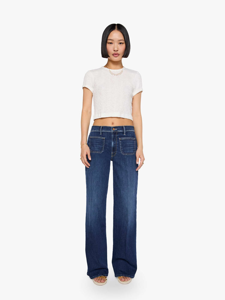 Front view of a woman in a dark blue mid-rise jeans with a loose fit, wide leg, patch pockets, zip fly and 29-inch inseam with a clean hem.