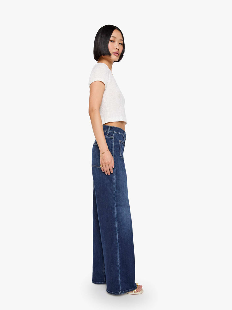 Side view of a woman in a dark blue mid-rise jeans with a loose fit, wide leg, patch pockets, zip fly and 29-inch inseam with a clean hem.
