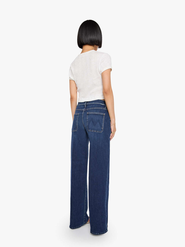 Back view of a woman in a dark blue mid-rise jeans with a loose fit, wide leg, patch pockets, zip fly and 29-inch inseam with a clean hem.