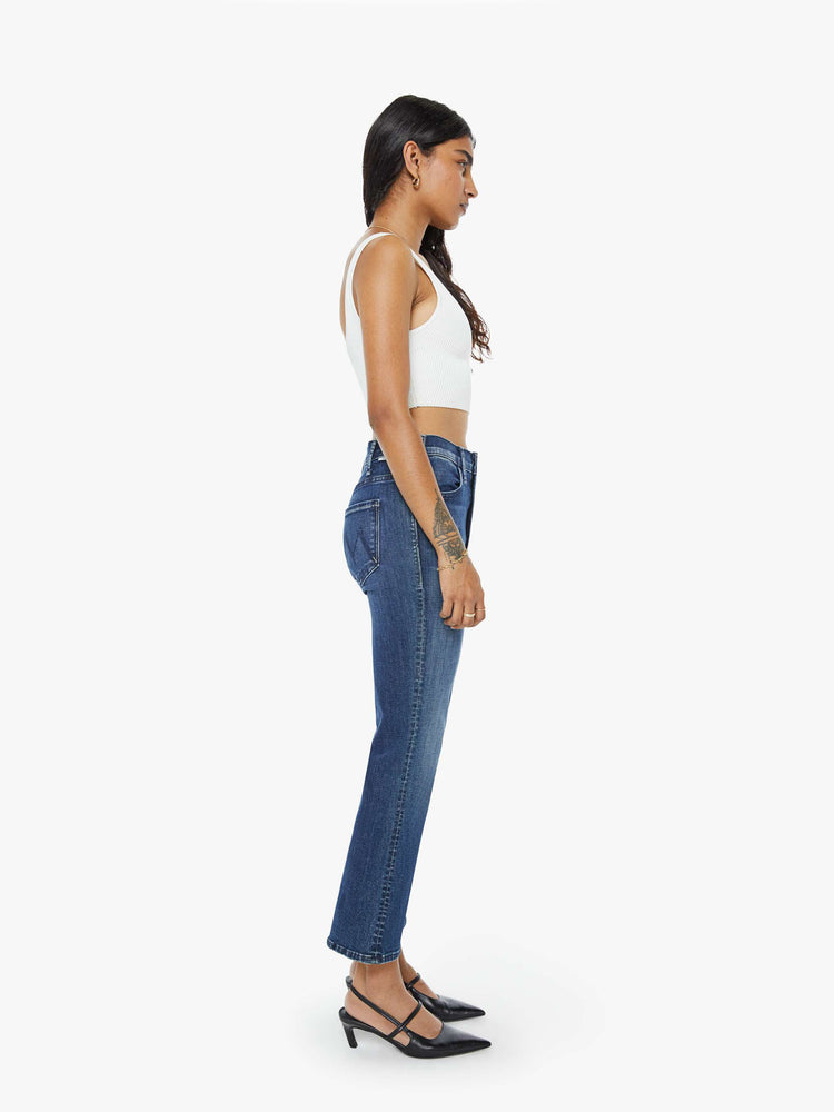 Side view of a petite woman in a dark blue wash high-rise flare has an ankle-length inseam and a clean hem. 