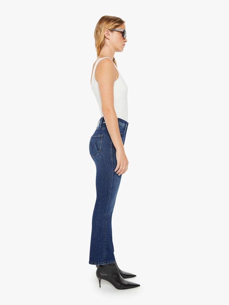 Side view of a petite woman in a dark blue wash high-rise flare has an ankle-length inseam and a clean hem.