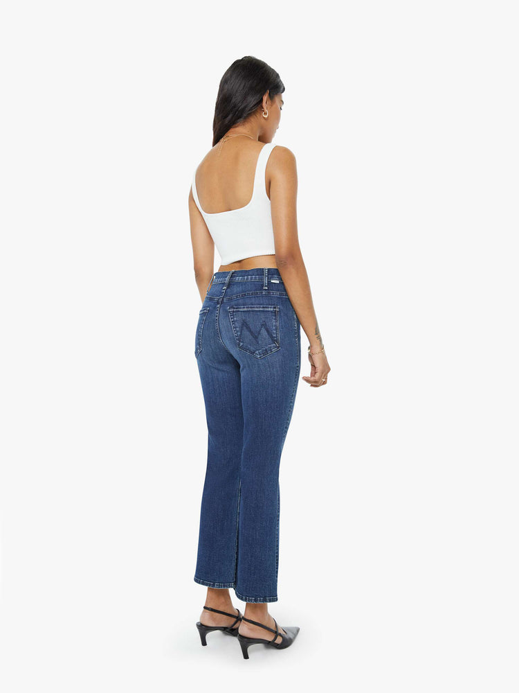 Back view of a petite woman in a dark blue wash high-rise flare has an ankle-length inseam and a clean hem. 