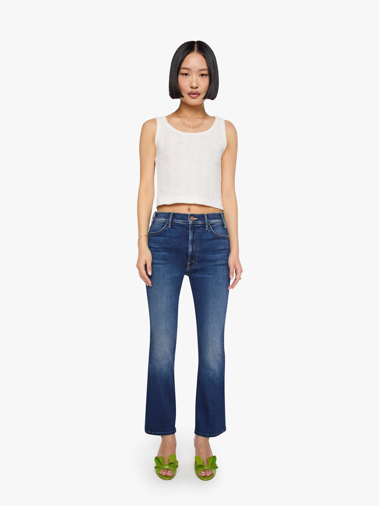 Front view of a petite woman in a dark blue  high-rise flare has an ankle-length inseam and a clean hem. 
