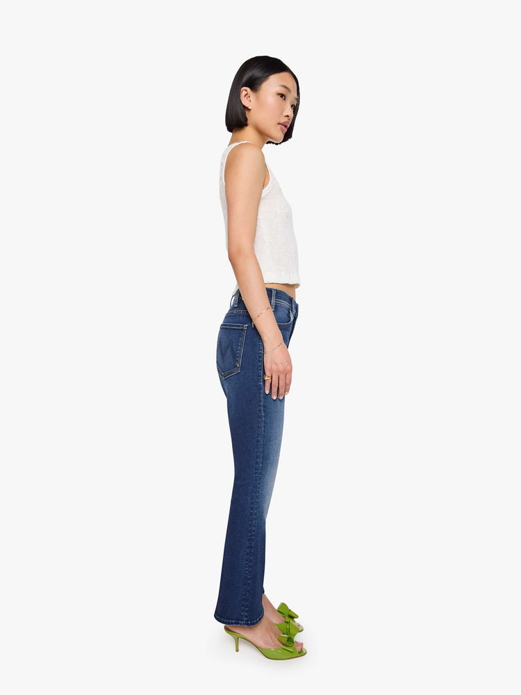 Side view of a petite woman in a dark blue  high-rise flare has an ankle-length inseam and a clean hem. 