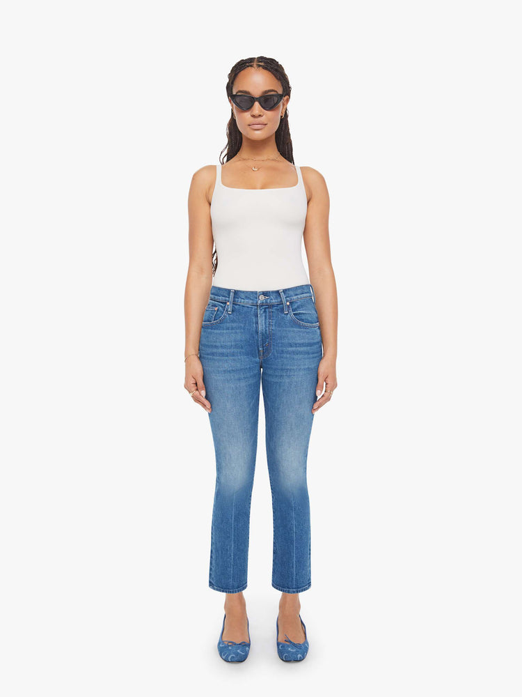 Front view of woman in a mid-blue jean with a high-rise bootcut has an ankle-length inseam, zip fly and a clean hem.