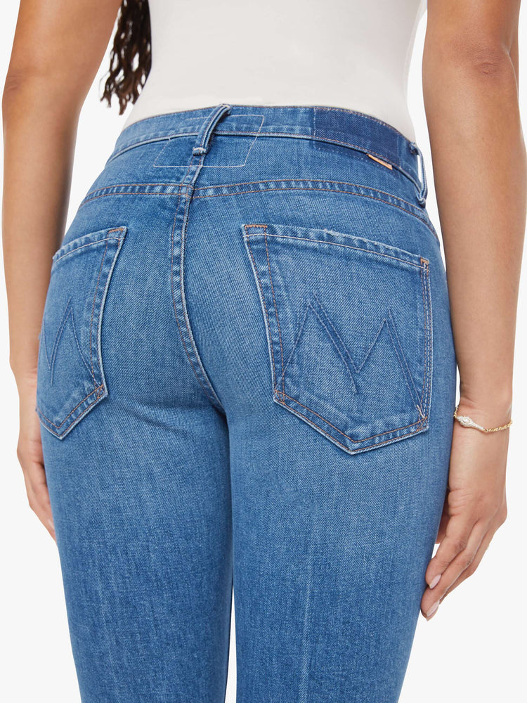 Close up view of woman in a mid-blue jean with a high-rise bootcut has an ankle-length inseam, zip fly and a clean hem.