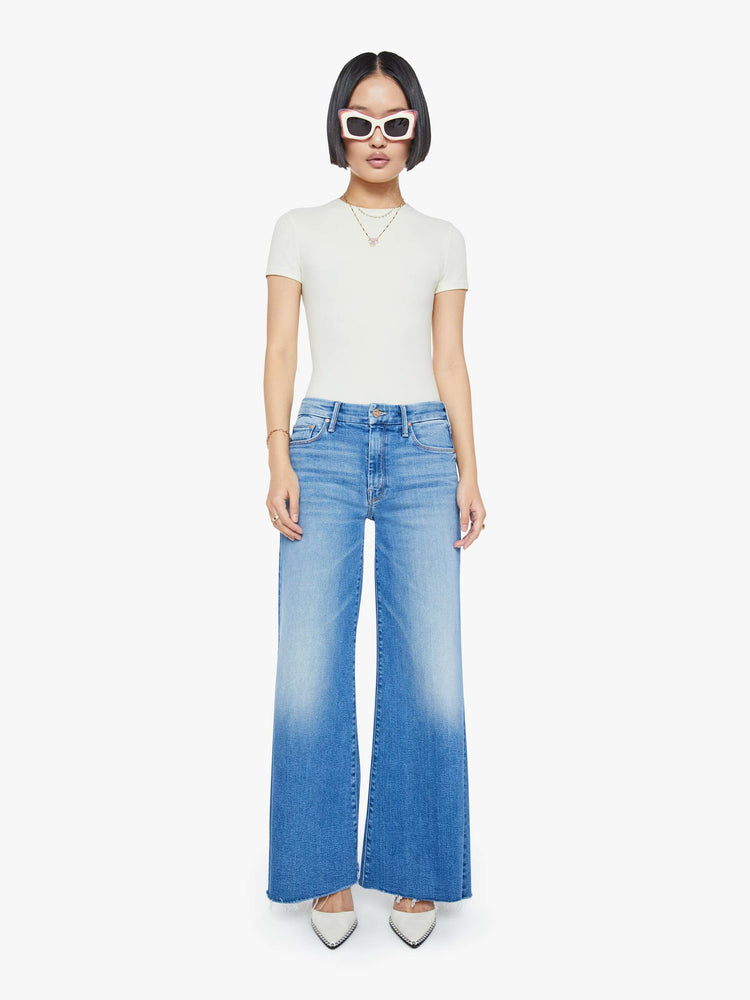 Front view of a petite woman in a mid blue high waisted wide leg jean with a 29-inch inseam and a frayed hem.
