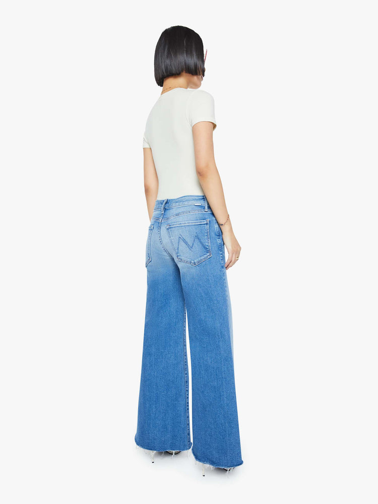 Back  view of a woman in a mid blue high waisted wide leg jean with a 29-inch inseam and a frayed hem.